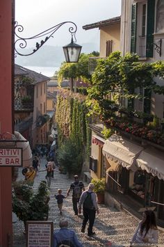 people are walking down an old cobblestone street with shops and restaurants on either side