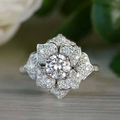 an engagement ring with diamonds in the center on a wooden table next to white roses