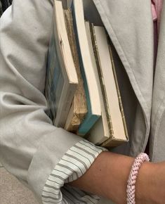 a person holding several books in their hands while wearing a pink bracelet and gray jacket