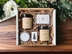 an open gift box containing three candles and two soaps on a table with flowers in the background