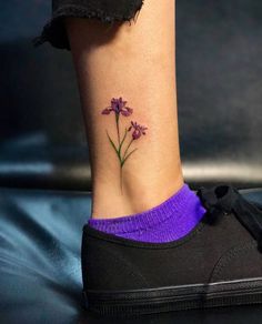 a small purple flower tattoo on the side of a woman's leg, with her foot