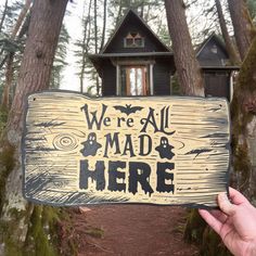 a hand holding up a sign that says we're all mad here in front of some trees