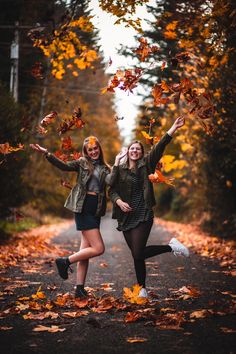 two young women are posing in the middle of an autumn forest with leaves falling from trees