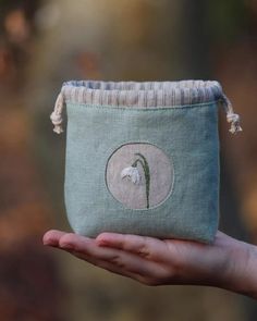 a hand holding a small pouch with a white flower on the front and green lining