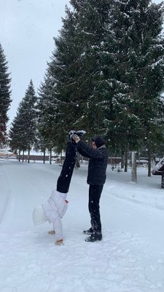 two people are playing in the snow near trees