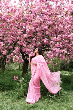 a woman in a pink sari standing under a flowering tree