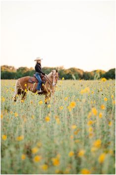 a woman riding on the back of a brown horse through a field of yellow flowers