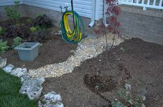 a garden area with gravel, rocks and a hose on the side of the house