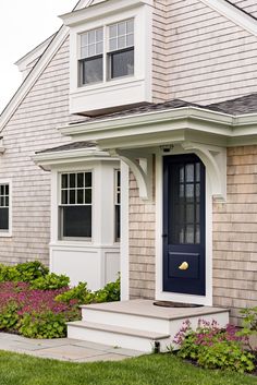 a blue door sits in front of a gray house with white trim and flowers on the lawn