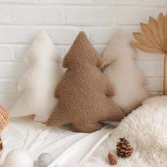 three pillows with different shapes and sizes on top of a white blanket next to a small tree