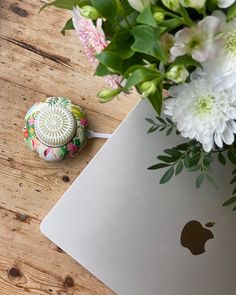 an apple laptop sitting on top of a wooden table next to a bouquet of flowers