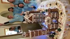 four people standing in front of a gingerbread house made out of cookies and marshmallows