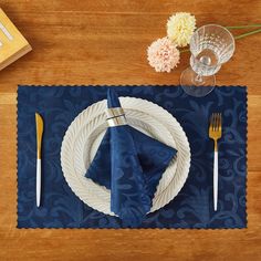 a place setting on a wooden table with blue and white napkins, silverware, and flowers