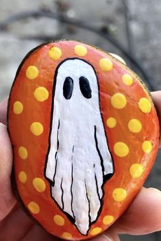 a hand holding a painted rock with a ghost face and yellow polka dots on it