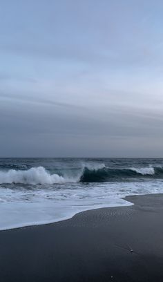 the ocean waves are coming in from the shore on a cloudy day at the beach