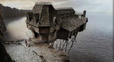 an old wooden house sitting on top of a cliff next to the ocean under a cloudy sky