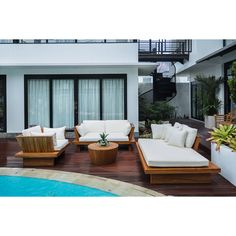 an outdoor living area with white couches and wooden tables next to a swimming pool