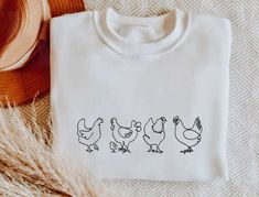 a t - shirt with three chickens on it and a straw hat next to it