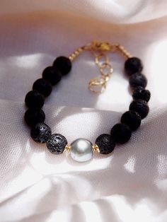 "Adorned with a mix of textured lava beads and a single black Tahitian pearl, this handmade beaded bracelet is a stylish personification of Hawaii's enigmatic allure. This stunning Tahitian pearl bracelet elegantly exemplifies mindful island living. Wear this alone or stacked for a classically elegant statement. ✦ DETAILS ✦ ✧ Name: Roselani (rose-LAH-nee) - Heavenly Rose. ✧ Adjustable Length from: 7\"-8.5\" ✧ Genuine Tahitian Pearl 8-10mm AA-AAA quality; tone and shape varies. ✧ 8mm Black Lava B Elegant Lava Stone Bracelets With Round Beads, Elegant Lava Stone Bracelet With Round Beads, Lava Bead Jewelry, Black Pearl Bracelet, Tahitian Pearl Bracelet, Pearl Beaded Bracelet, Hawaii Jewelry, Crystal Bead Jewelry, Lava Bead Bracelet