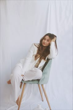 a woman sitting on top of a green chair next to a white wall in front of a white backdrop