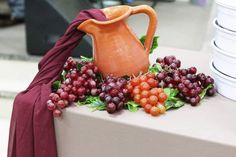 a table topped with plates and a vase filled with grapes