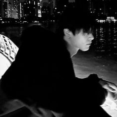 a man sitting on top of a bench next to a body of water at night