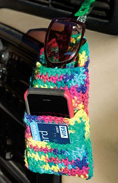 a cell phone and sunglasses in a colorful pouch on a car seat belt with a keychain attached to it