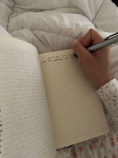 a person writing in a notebook with a pen on top of the book and an open notepad next to it