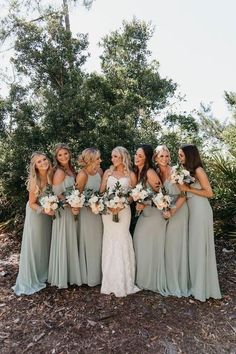 a group of women standing next to each other in front of some trees and bushes