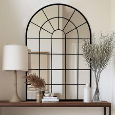 a table with a mirror, vases and lamp on it in front of a white wall