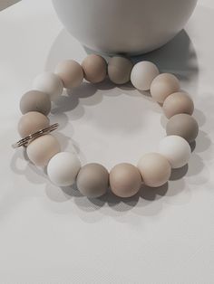 a white and beige beaded bracelet next to a bowl