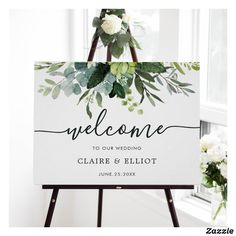 a welcome sign with greenery and white flowers on it is displayed in front of a window