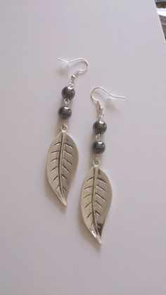 the earrings are made with silver beads and leaf shaped pendants on top of each other