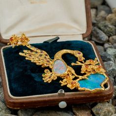 This stunning pendant features a bird and flower design, bezel set with two (2) opal cabochons. The flowers are each four-prong set with one (1) round mixed cut hessonite garnet. The eye of the bird is flush set with one (1) round mixed cut ruby. The feathers of the bird are flush set with a total of twenty- five (25) round mixed cut tourmaline and seventeen (17) round mixed cut demantoid garnets. The pendant measures 90.0mm long, including the bail and 40.0mm wide. The chain in the photo is not Elegant Multi-stone Opal Jewelry, Luxury Hallmarked Opal Jewelry, Luxury Opal Cabochon Jewelry, Exquisite Collectible Jewelry Brooch, Exquisite Collectible Brooch Jewelry, Bird And Flower, Gemstone List, Demantoid Garnet, Brand Presentation