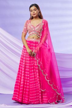 Hot pink pleated lehenga with attached cancan, in georgette base with tie and dye pattern and embroidered waistband. Comes with a mirror work, glass beads and shell tassel embroidered choli cut padded blouse and a scalloped mirror work organza dupatta. Component: 3 Pattern: Tie and Dye, Embroidered Type Of Work: Leheriya Pattern, Mirror, Glass Beads, Shell Work Neckline: Plunged V-Neck Sleeve Type: Half Fabric: Lehenga and Blouse - Georgette with Shantoon Lining, Dupatta- Organza Color: Pink Oth Indian Silk Dresses, Pleated Lehenga, Lehenga And Blouse, Scalloped Mirror, Mehendi Outfits, Lehenga Designs Simple, India Dress, Padded Blouse, Pink Lehenga