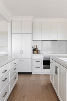 an all white kitchen with wood floors and cabinets in the middle is seen from across the room