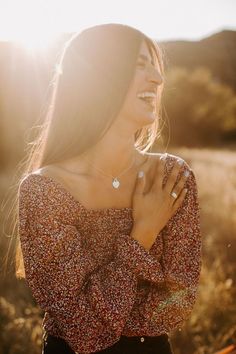 a woman standing in a field with her hands on her chest and smiling at the camera