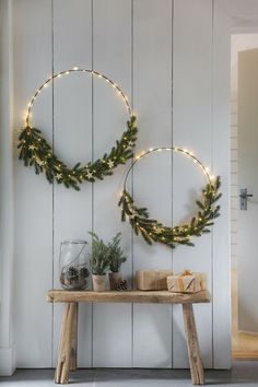 two christmas wreaths are hanging on the wall above a table with presents and candles