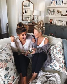 two women sitting on a couch holding wine glasses in their hands and laughing at each other