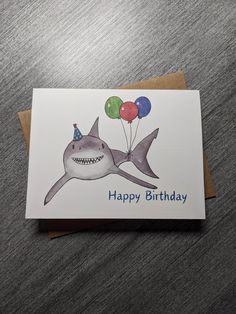 a birthday card with a shark holding balloons