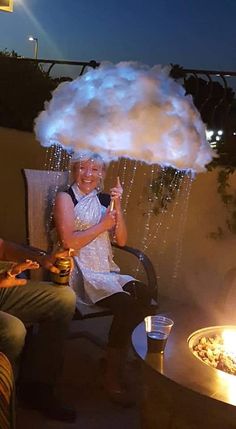 a man and woman sitting in chairs under an umbrella with clouds on top of them