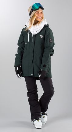 a woman wearing a green jacket and black snowboard pants, standing in front of a gray background