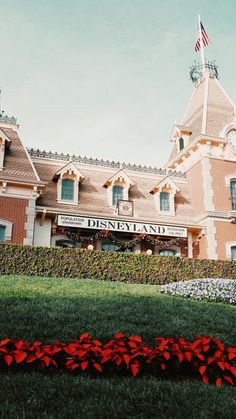 the disneyland land building has red flowers in front of it and an american flag on top