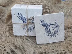 two square coasters with blue designs on them sitting on a burlocked cloth