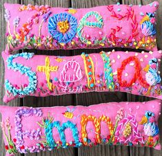 two pink embroidered pillows sitting on top of a wooden table