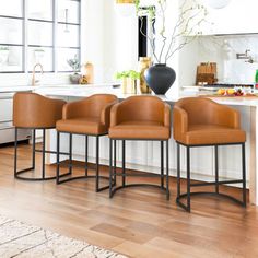 four brown leather chairs sitting on top of a wooden floor next to a kitchen island