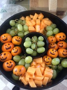 a bowl filled with grapes, oranges and green grapes topped with carved pumpkin faces