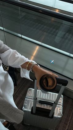 a woman sitting on top of a metal chair next to an airport luggage bag in front of a window