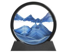 a blue and white glass sculpture with mountains in the background on a black stand against a white backdrop