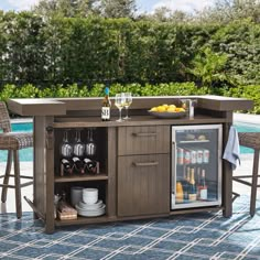 an outdoor bar with wine glasses and bottles on it next to a swimming pool, surrounded by wicker chairs